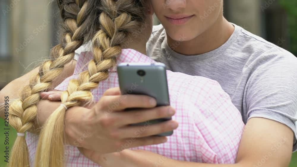 Boy texting on smartphone while embracing girlfriend, lie and betrayal, closeup