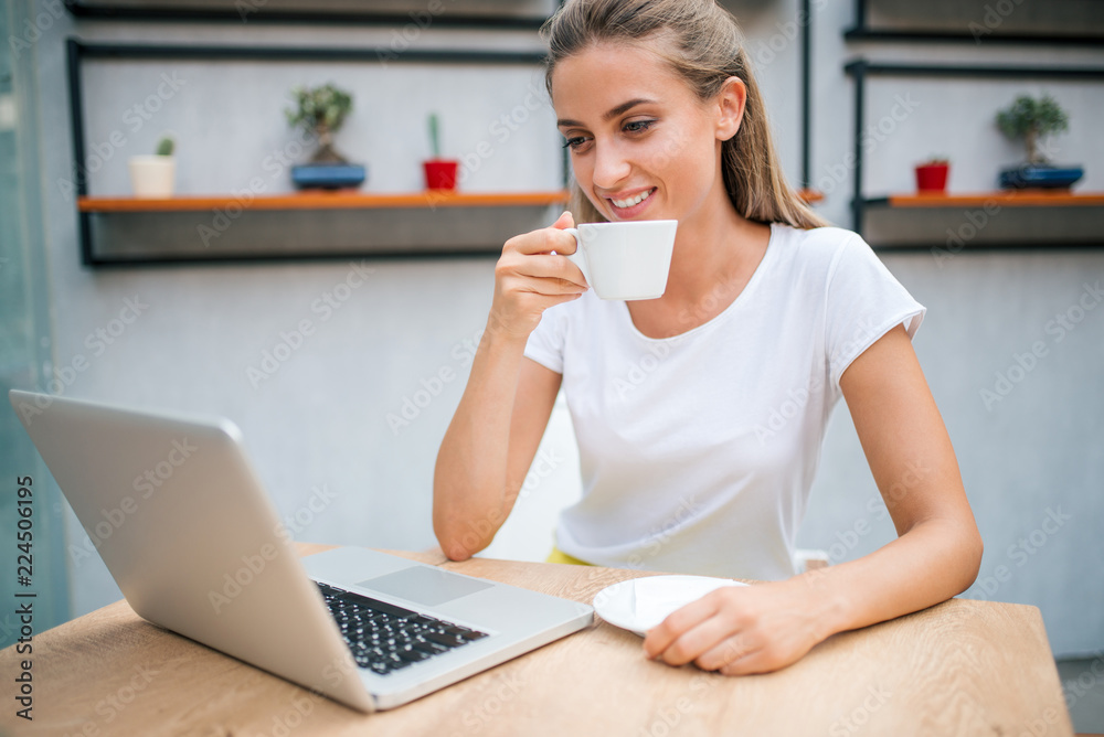 Smiling girl drinking coffee and using laptop indoors. Smiling girl drinking coffee and using laptop indoors.