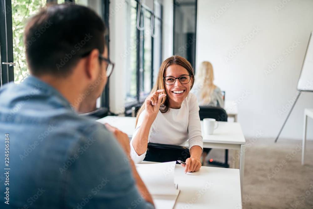 Cheerful young woman talking while sitting at desk during class at college or university. Cheerful young woman talking while sitting at desk during class at college or university.