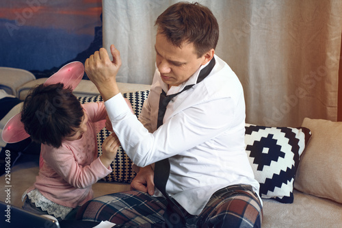 Littlr daughter helping father to button white shirt. Sitting on sofa. Father preparing for meeting. photo