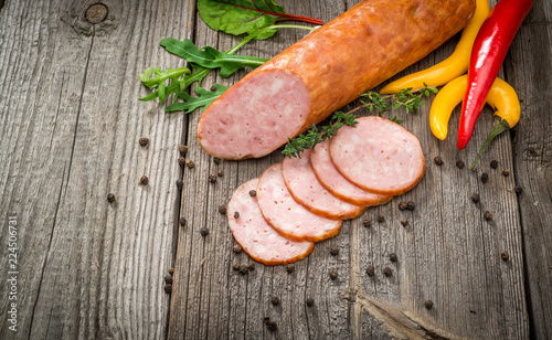 Salami sausages sliced with pepper, garlic and rosemary on cutting board on wooden table. Top view