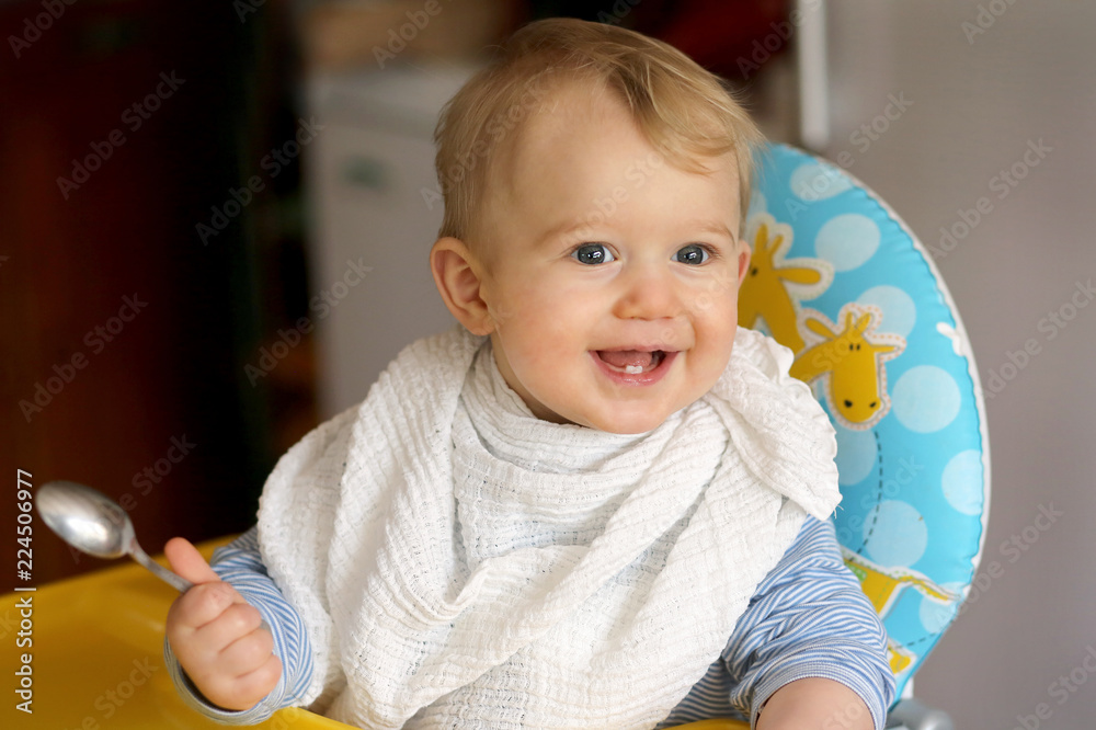 Petit bébé garçon blond assit dans sa chaise haute pret à manger avec la  petite cuillere dans la main Stock Photo | Adobe Stock