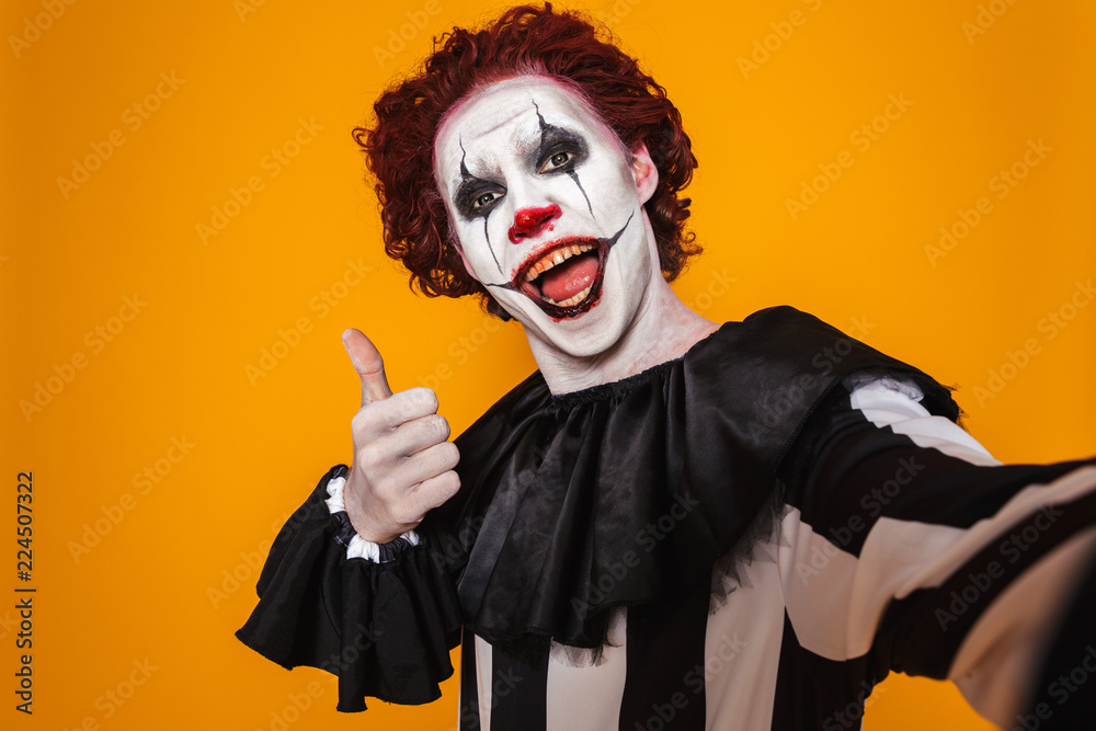 Excited clown man 20s wearing black costume and halloween makeup looking at  camera, isolated over yellow background Stock Photo | Adobe Stock