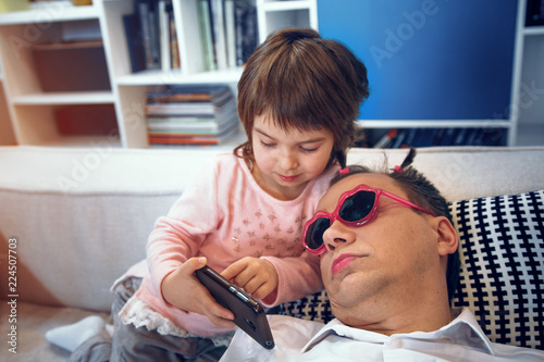 Little girl making selfie with her sleeping father.Made tails on his head and put funny sunglasses.