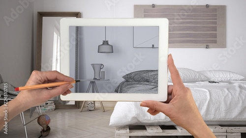 Hands holding and drawing on tablet showing modern living room CAD sketch. Real finished minimalist bedrom in the background, architecture interior design presentation photo