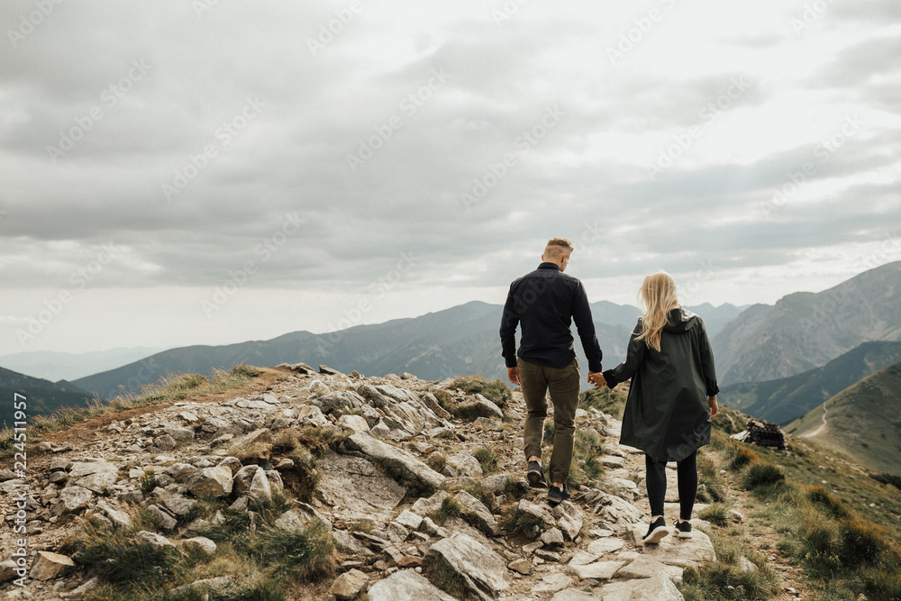 Couple travelers woman and man follow holding hands at mountains with landscape on background. happy emotions. Lifestyle concept. Young family traveling active adventure vacations Couple travelers woman and man follow holding hands at mountains with landscape on background. happy emotions. Lifestyle concept. Young family traveling active adventure vacations