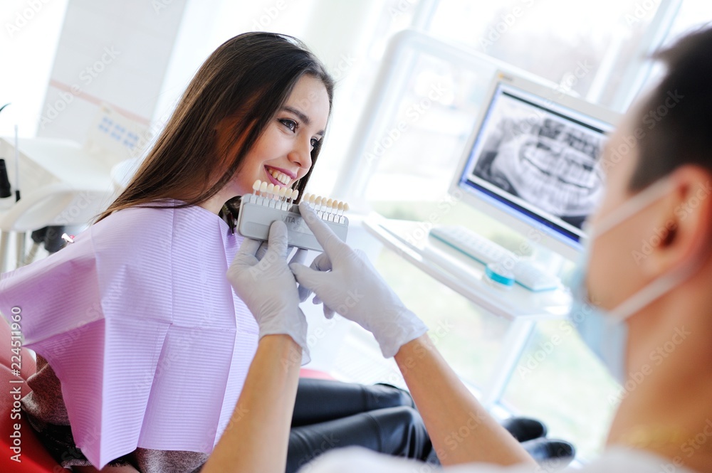 The dentist selects a young pretty girl for the patient a shade of teeth and shows on the monitor an x-ray of teeth. The dentist selects a young pretty girl for the patient a shade of teeth and shows on the monitor an x-ray of teeth.