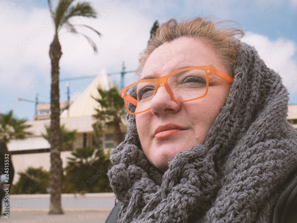 Portrait of calm mature woman in street with orange glasses and scarf with palm tree and blue sky in background. Vintage picture concept