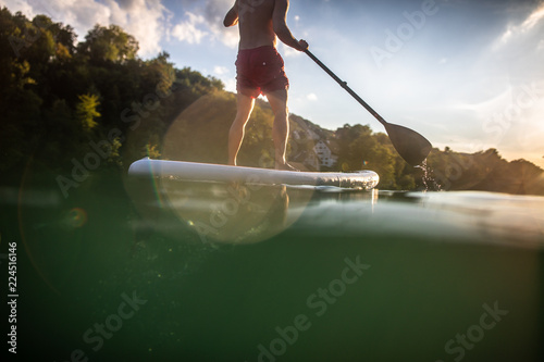 Handsome young man on a paddle board. Getting a great exercise on a lovely river in warm evening sunlight photo