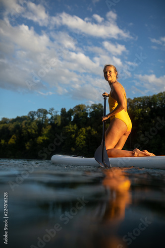 SUP Stand up paddle board concept - Pretty  young woman paddle boarding on a lovely lake in warm late afternoon light - shot from underwater
