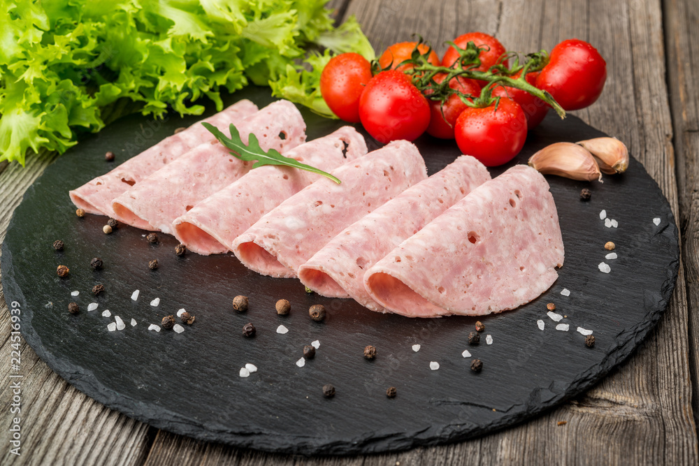 Cut sausage from ham on a wooden background