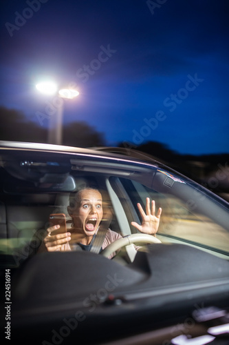 Young female driver playing with her cellphone instead of paying attention to driving startled in a potentially dangerous situation - Road safety concept photo