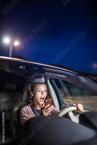Young female driver playing with her cellphone instead of paying attention to driving startled in a potentially dangerous situation - Road safety concept