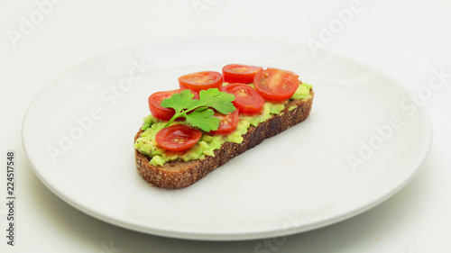Avocado Toast with Tomatoes and Parsley on a White Plate on a White Background.