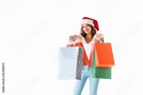 attractive smiling girl in santa hat holding shopping bags, isolated on white