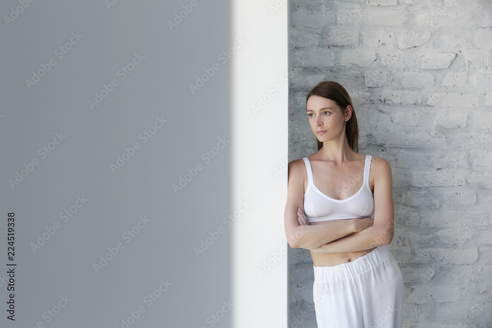 Young beautiful woman in casual cotton outfit leaning on the wall, indoor portrait, calm morning concept in the yoga studio Young beautiful woman in casual cotton outfit leaning on the wall, indoor portrait, calm morning concept in the yoga studio