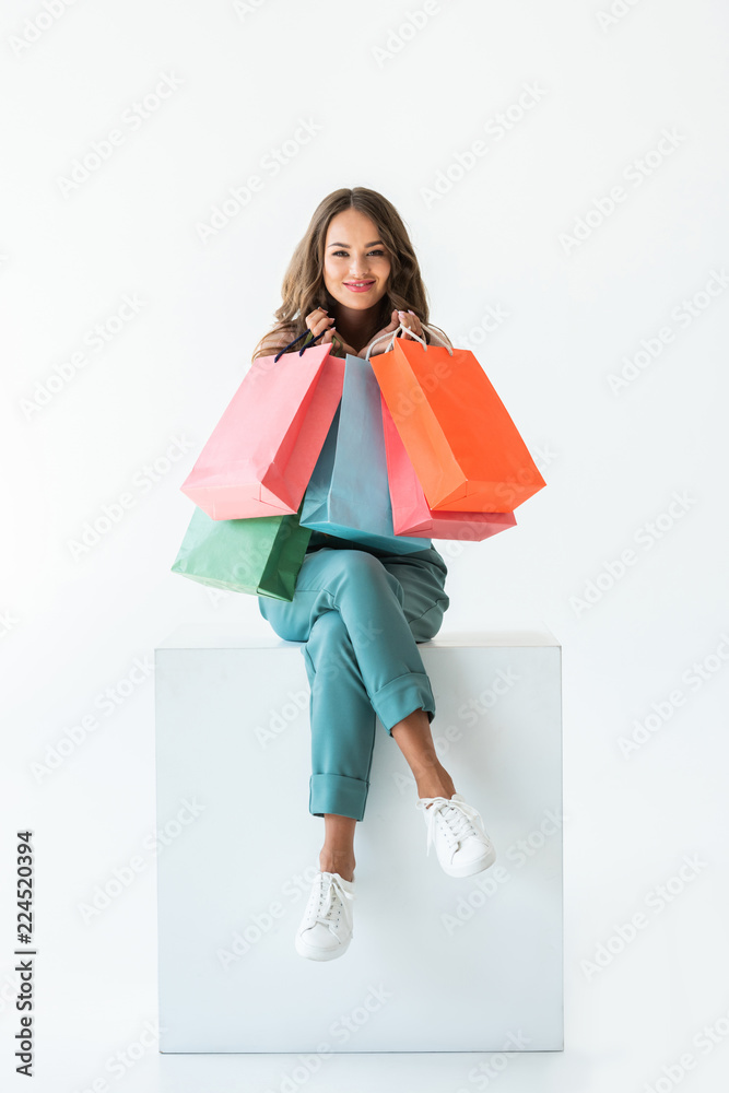 smiling shopaholic sitting on white cube with shopping bags, isolated on white smiling shopaholic sitting on white cube with shopping bags, isolated on white