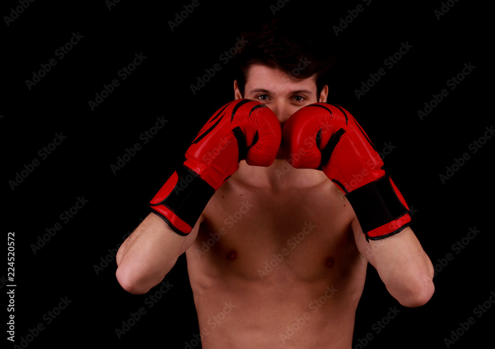 Muscular young handsome man wearing box gloves and punching in front of black background