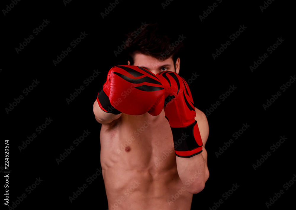 Muscular young handsome man wearing box gloves and punching in front of black background