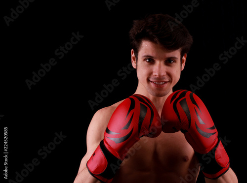 Muscular handsome young man with box gloves in front of black background © buraktumler