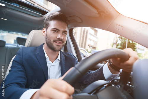 Portrait of joyful man driving car in formalwear and keeping han