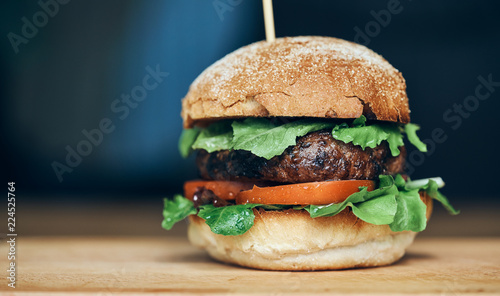 A beef burger in a crusty bun with lettuce and tomatoes on a cho
