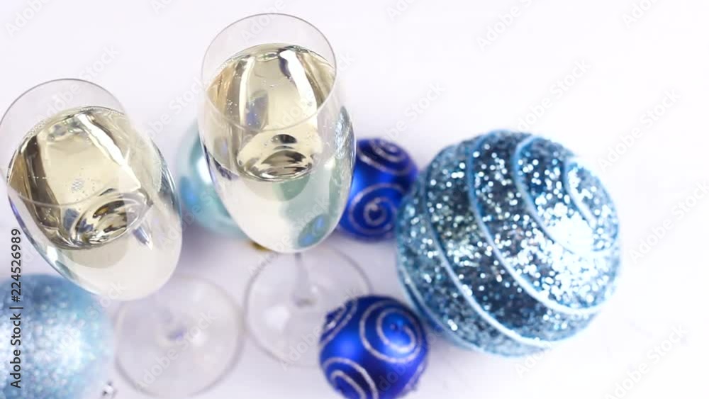 Two glasses of champagne with blue and silver christmas toys and decorations on white background. Two glasses of champagne with blue and silver christmas toys and decorations on white background.