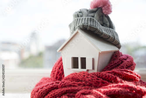 house in winter - heating system concept and cold snowy weather with model of a house wearing a knitted cap photo