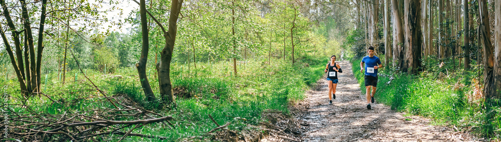 Young woman and man participating in a trail race through the forest Young woman and man participating in a trail race through the forest