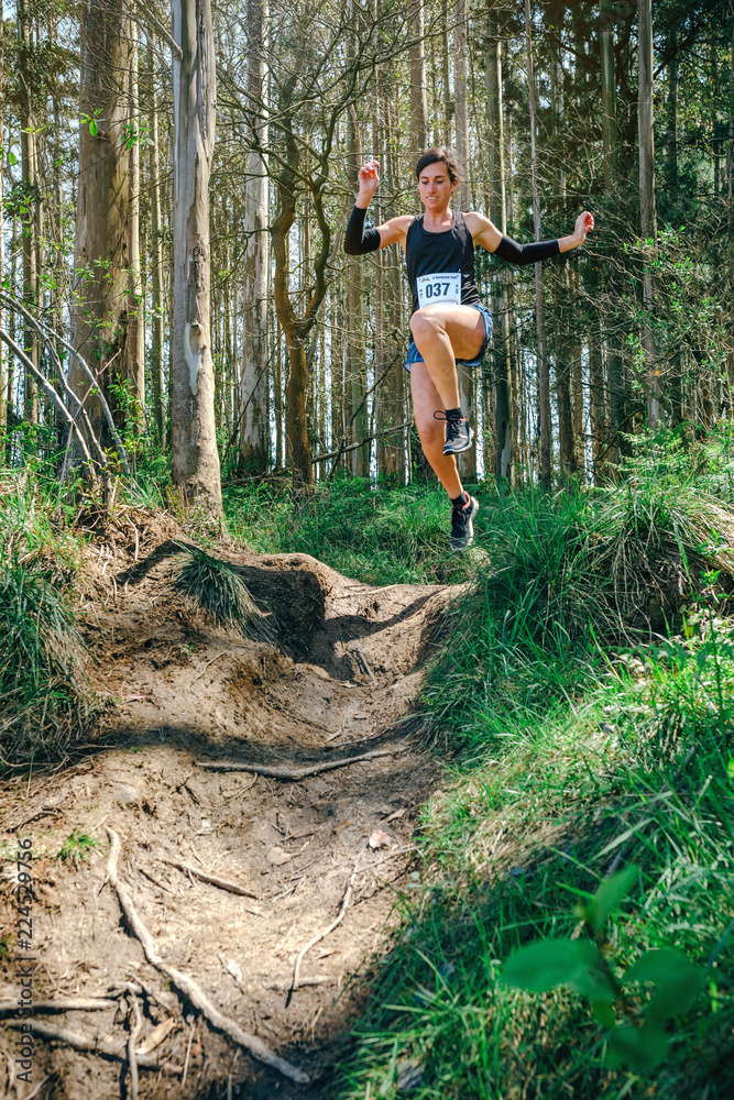 Naklejka premium Young woman jumping participating in a trail race through the forest