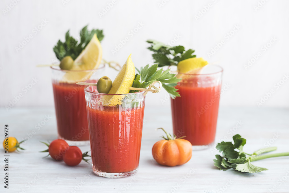 Glasses of fresh spicy tomato juice with celery garnished with lemon slice, green olive and parsley Glasses of fresh spicy tomato juice with celery garnished with lemon slice, green olive and parsley