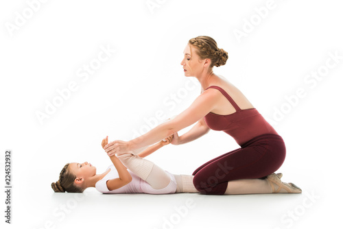 confident female trainer helping little ballerina stretching isolated on white background