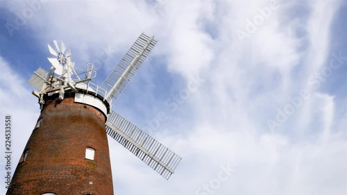 Old English Windmill. A low angle view of a traditional old English windmill in a gentle breeze set against a cloudy blue sky with space for copy.