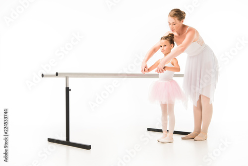 female teacher in tutu helping little ballerina practicing at ballet barre stand isolated on white background