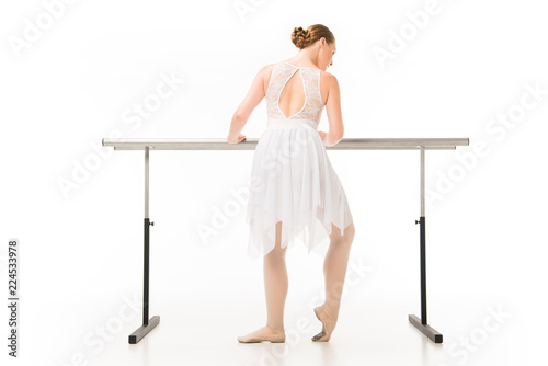 rear view of adult ballerina in tutu exercising at ballet barre stand isolated on white background