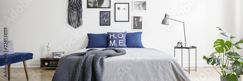 Real photo of a navy blue bedroom interior with a double bed, pillows and graphics on a wall