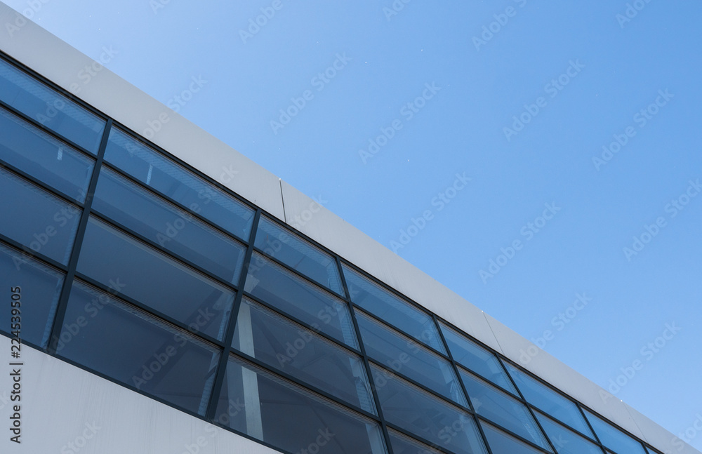 Building with white aluminum facade with windows and aluminum panels against blue sky.