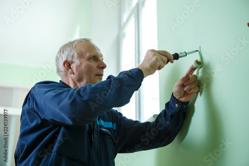 middle-aged senior man worker is working indoors fixing fitting screwing repairing