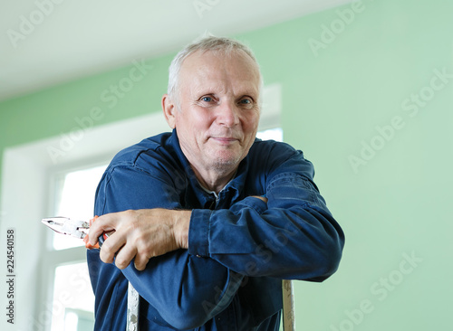 middle-aged senior man worker is working indoors fixing fitting screwing repairing
