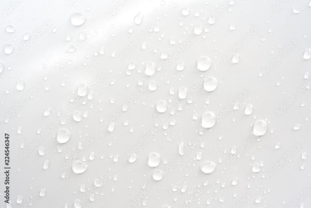 Rain drops on glossy white car hood surface of window at early night in rainy season - nature abstract background
