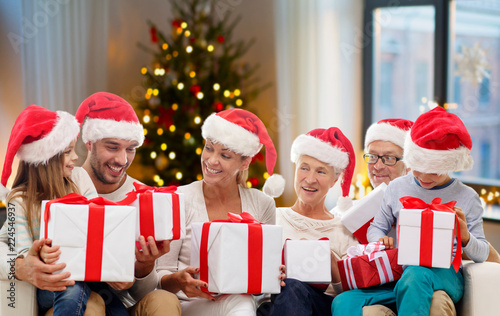 christmas, holidays and people concept - happy family in santa hats with gifts sitting on couch at home