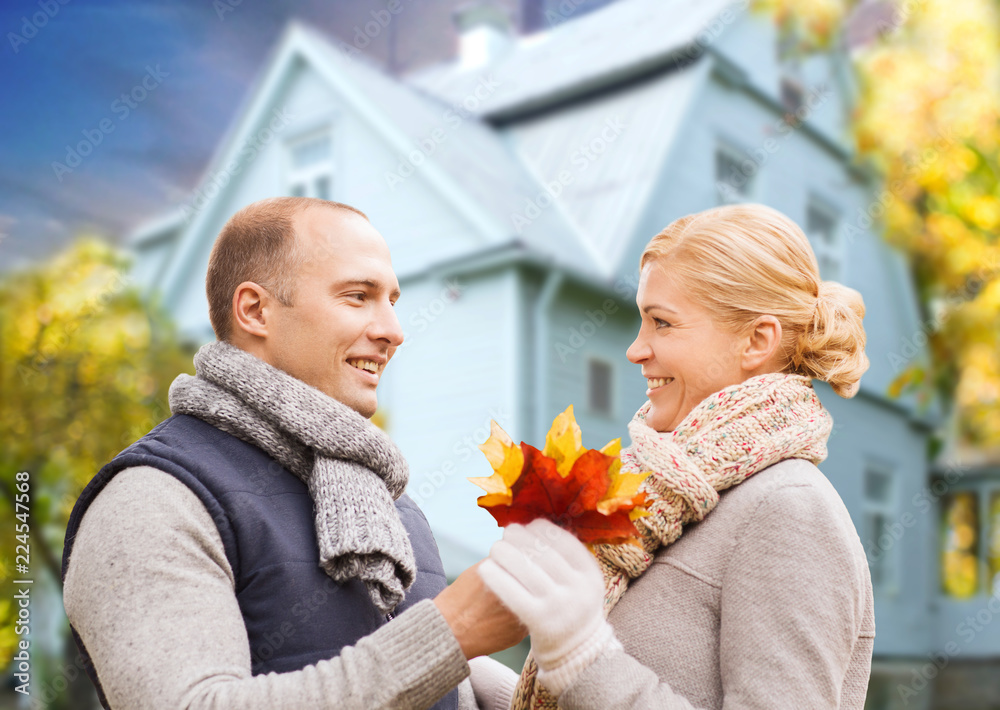 love, relationships and real estate concept - smiling couple with autumn maple leaves over living house background love, relationships and real estate concept - smiling couple with autumn maple leaves over living house background