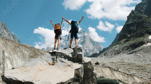 Obraz na plátně Couple of tourists with backpacks in the campaign raise their hands up on the top of the mountains