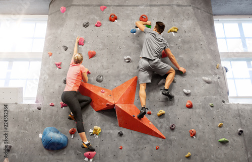 fitness, extreme sport and healthy lifestyle concept - young man and woman bouldering on a rock climbing wall at indoor gym