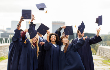 education, graduation and people concept - group of happy international students in bachelor gowns throwing mortar boards up in the air