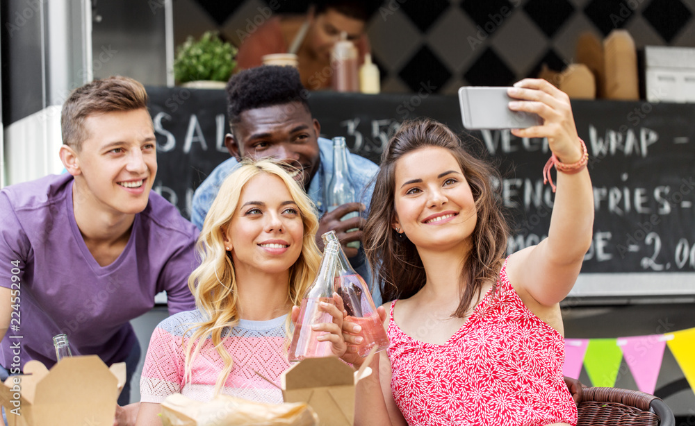 Obraz premium leisure and people concept - happy young friends with food and non alcoholic drinks and taking selfie at food truck