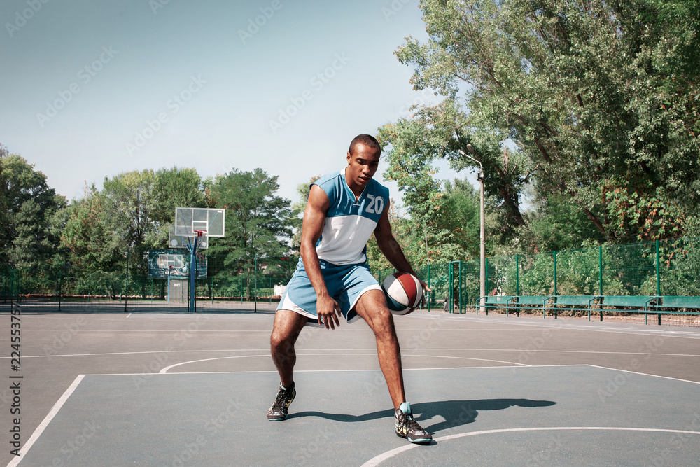 Fototapeta premium Picture of young confused african basketball player practicing outdoor. Fit afro man in motion and movement. athletic and sport lifestyle concept