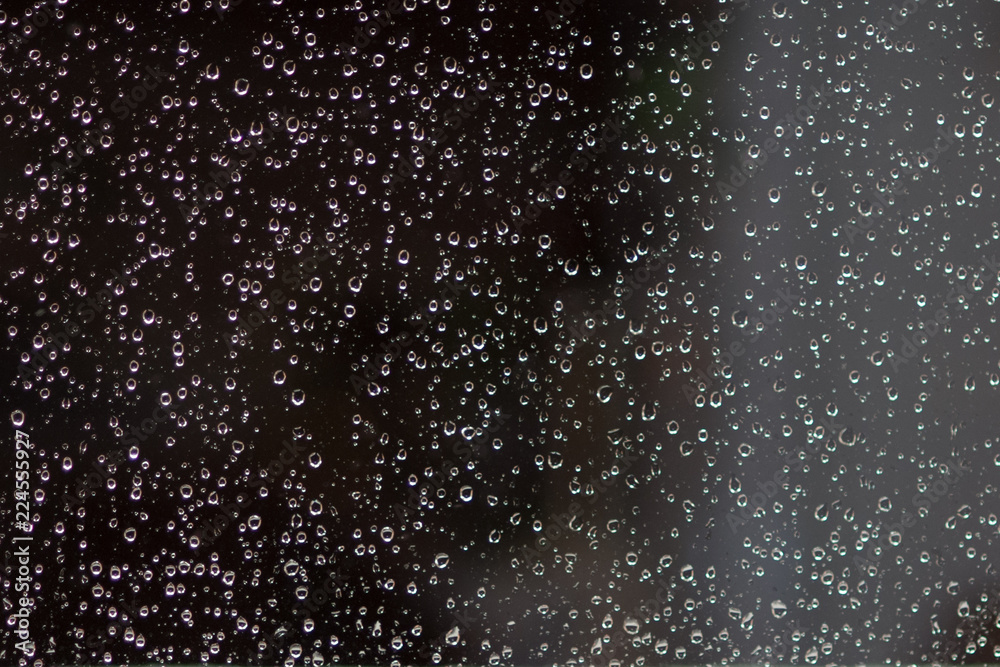 Rain drops on the window glass at night time.