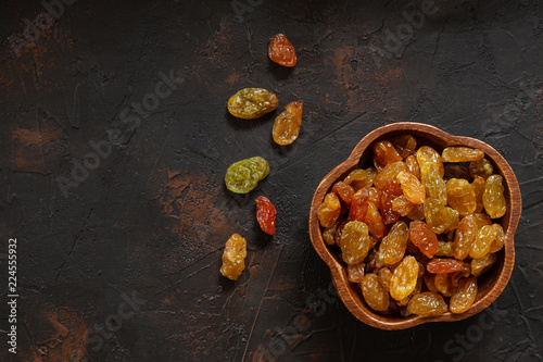 Organic dried golden raisins in wooden bowl on vintage dark background. Top view, close-up.