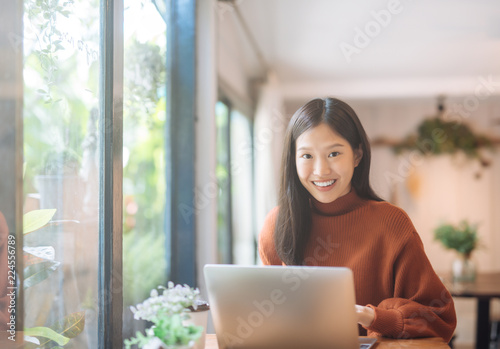 Happy young Asian girl working at a coffee shop with a laptop looking at camera.